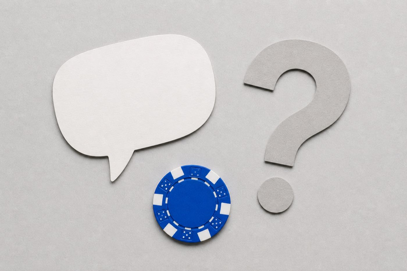 A speech bubble, a question mark and a single poker chip arranged on a table, representing frequently asked questions
